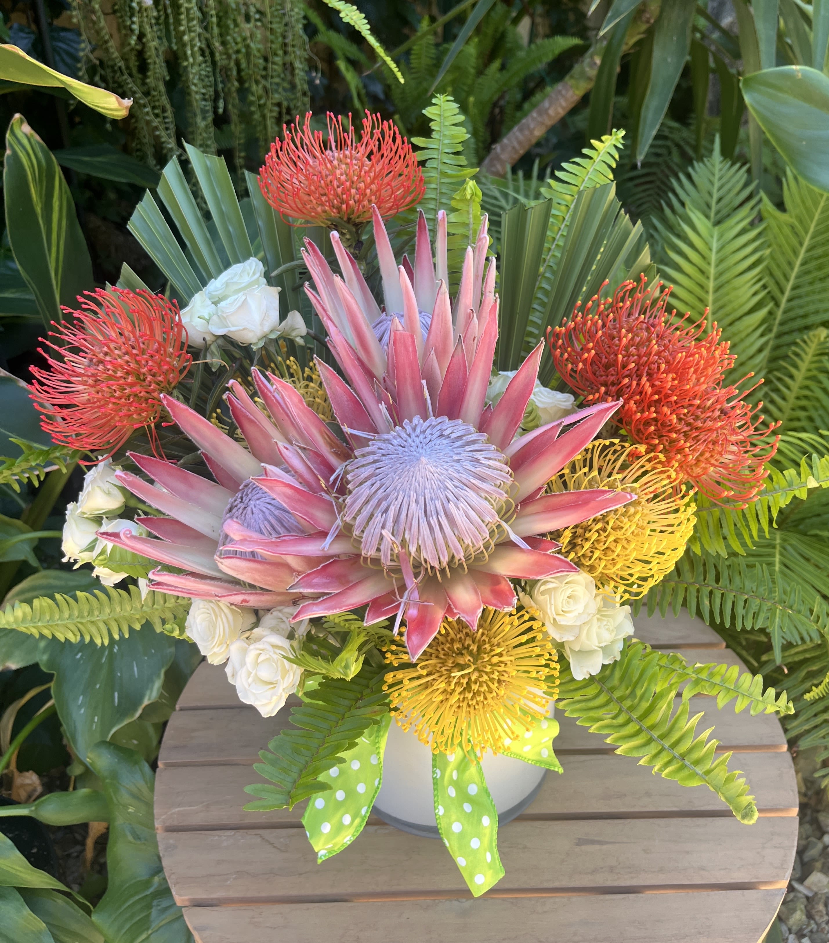 Tropical bouquet with pink protea, orange pincushion blooms, and white roses in a vase
