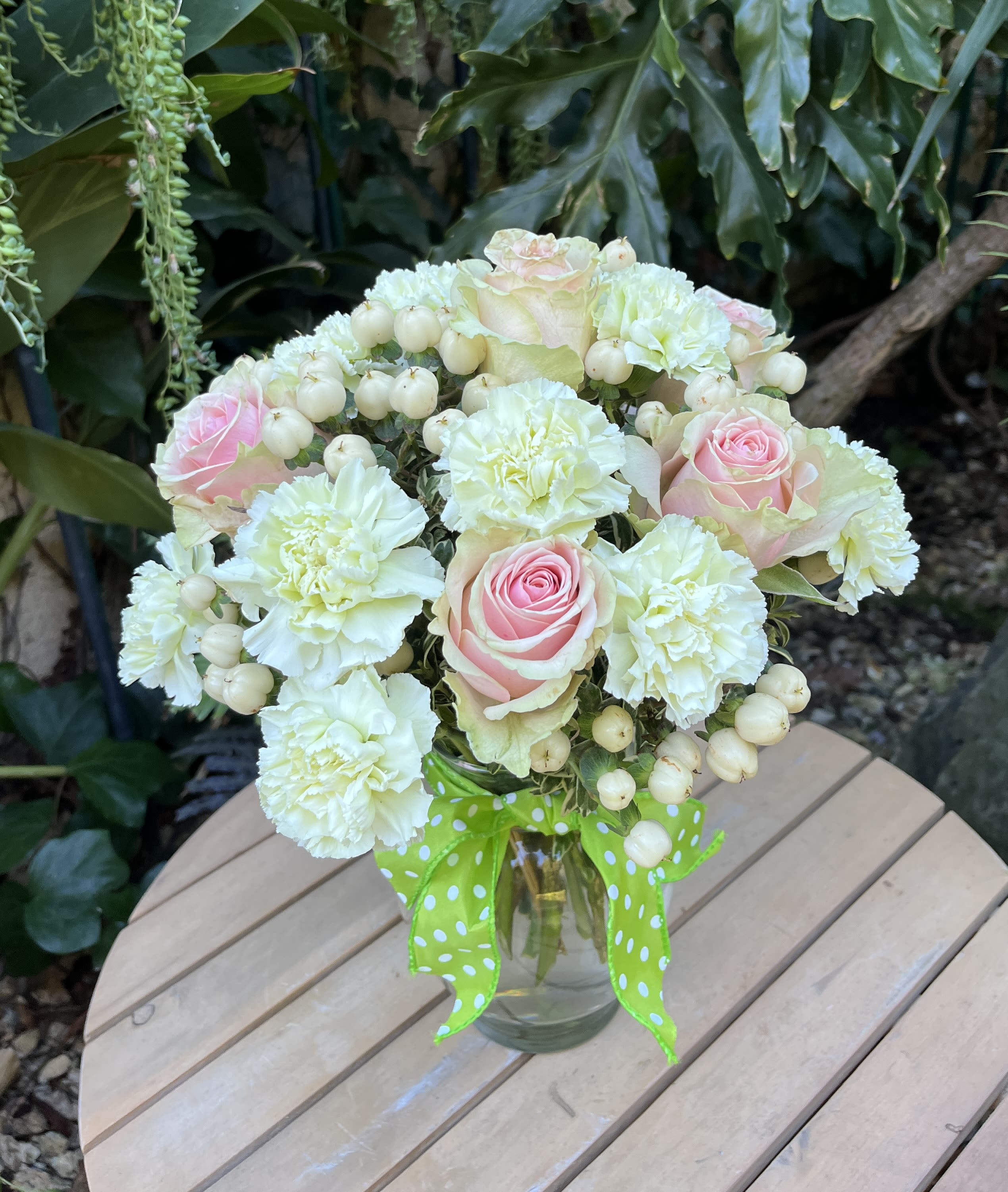 Bouquet of pink roses and white carnations in a glass vase with a green ribbon