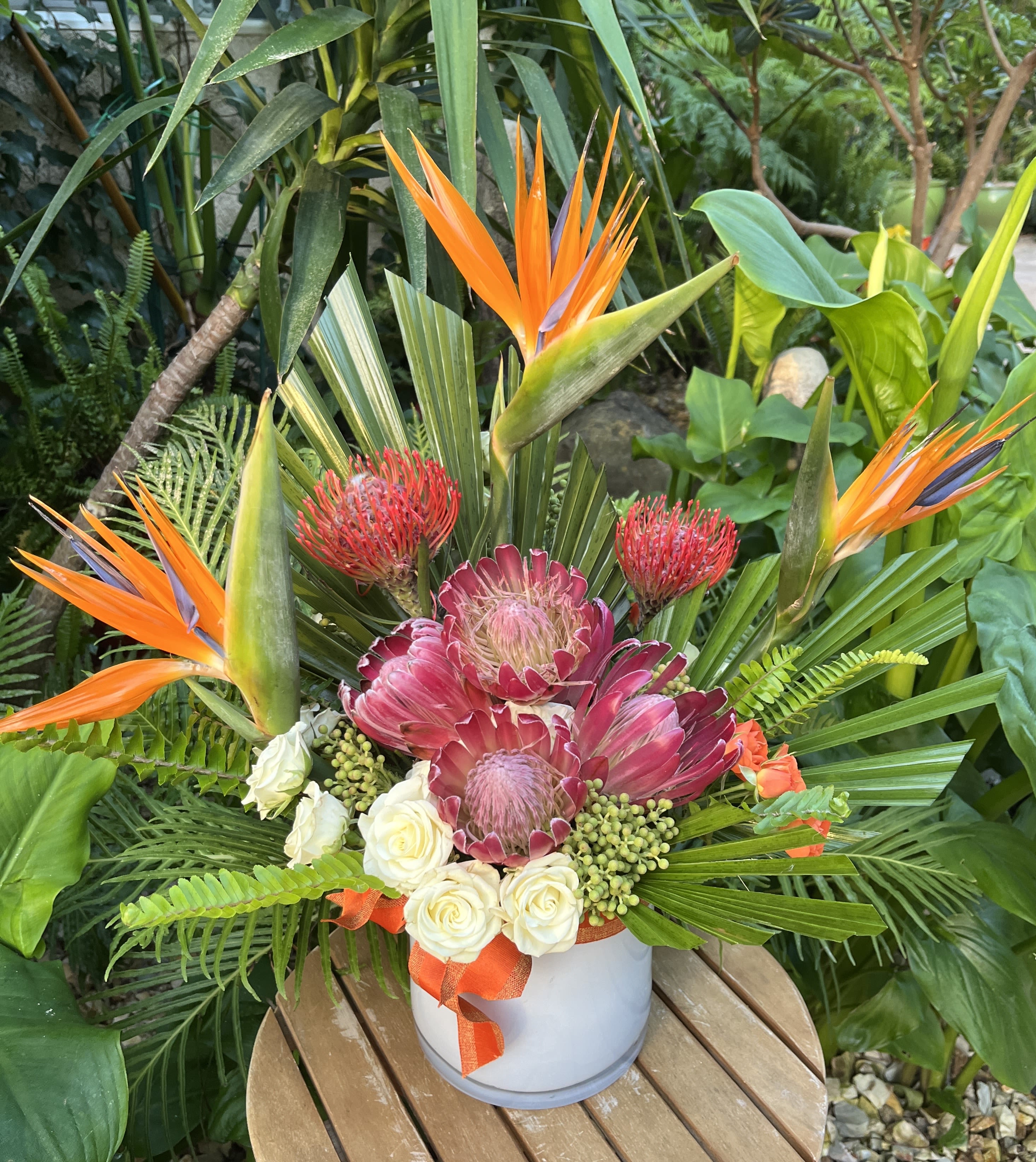 Tropical flower arrangement in a white vase with orange bird-of-paradise and pink protea