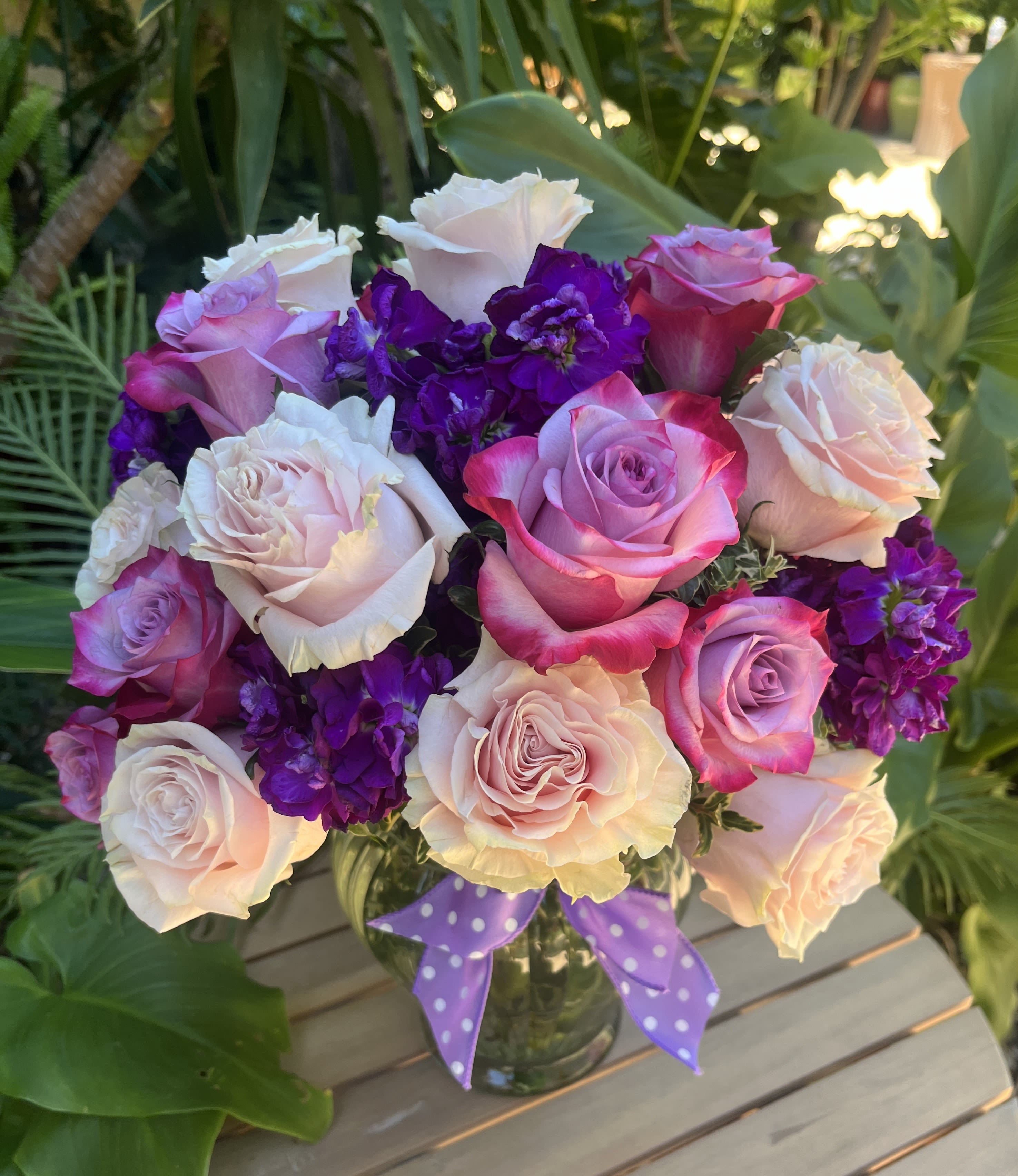 Bouquet of pink, white, and purple roses in a glass vase with a polka-dot ribbon