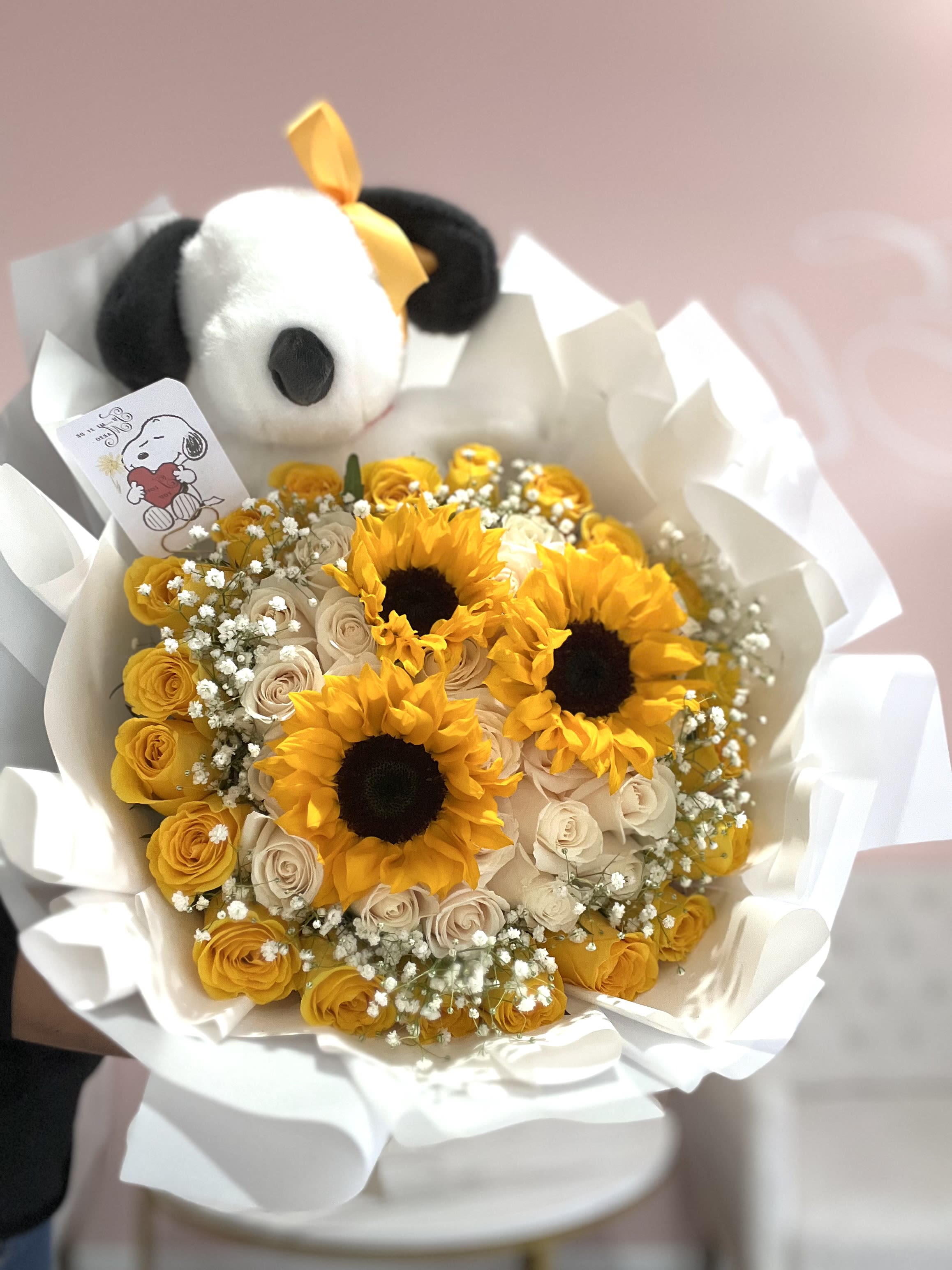 Bouquet of yellow sunflowers and pale roses with a plush panda topper
