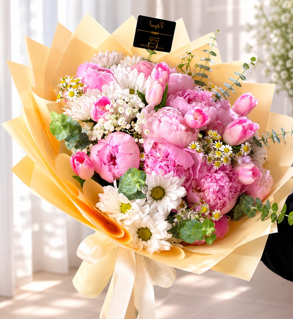 Peony Dream - Elegant hand-tied bouquet featuring 10 pink peonies and 10 pink tulips, beautifully accented with delicate white daisies, charming chamomile flowers, and fresh eucalyptus greenery. The combination creates a soft, romantic, and garden-inspired design full of texture and natural beauty. Wrapped in light pastel yellow Korean-style paper, this bouquet offers a refined and modern presentation, finished with a graceful ribbon for an extra touch of elegance. 