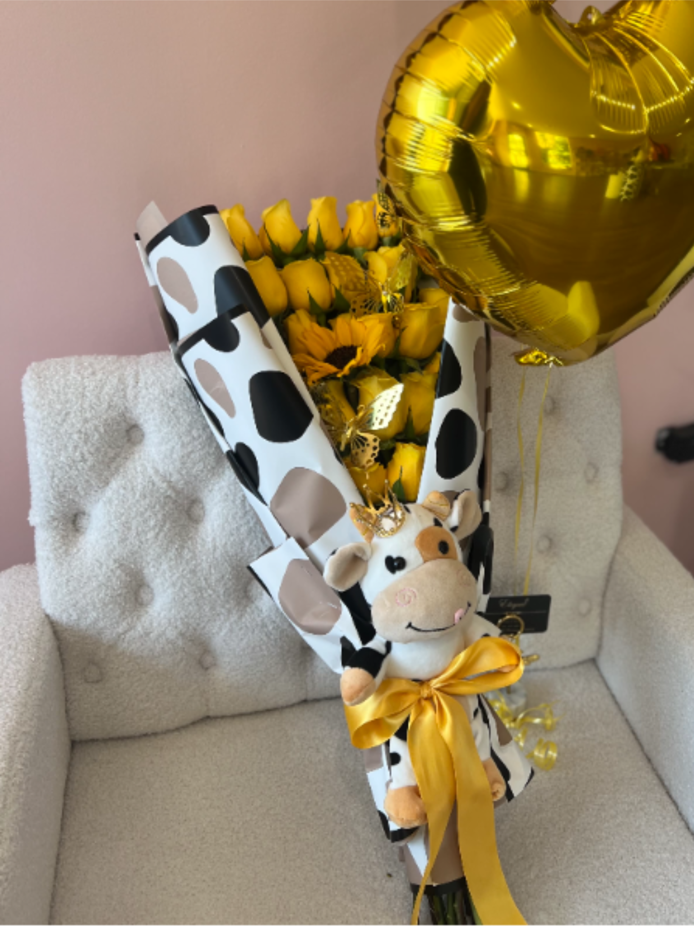 Bouquet of yellow roses and sunflowers with a plush cow and gold heart balloon on a chair