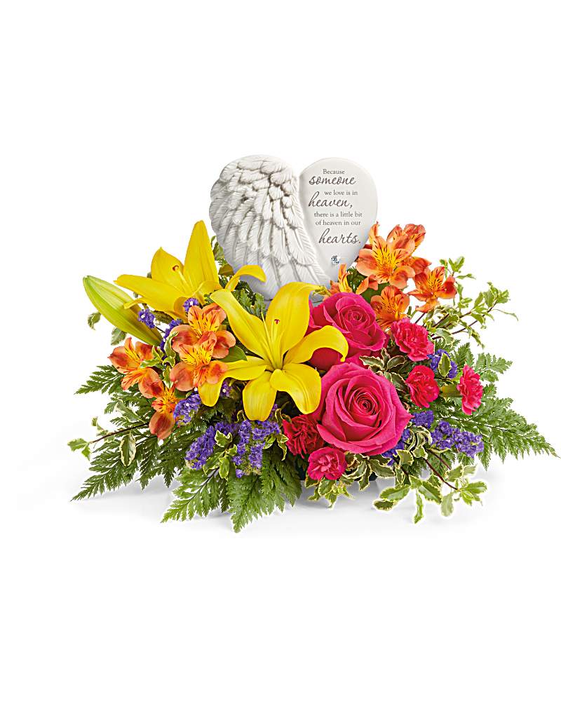 Low arrangement of yellow lilies, bright pink roses, and mixed blooms with a white angel wing heart keepsake.