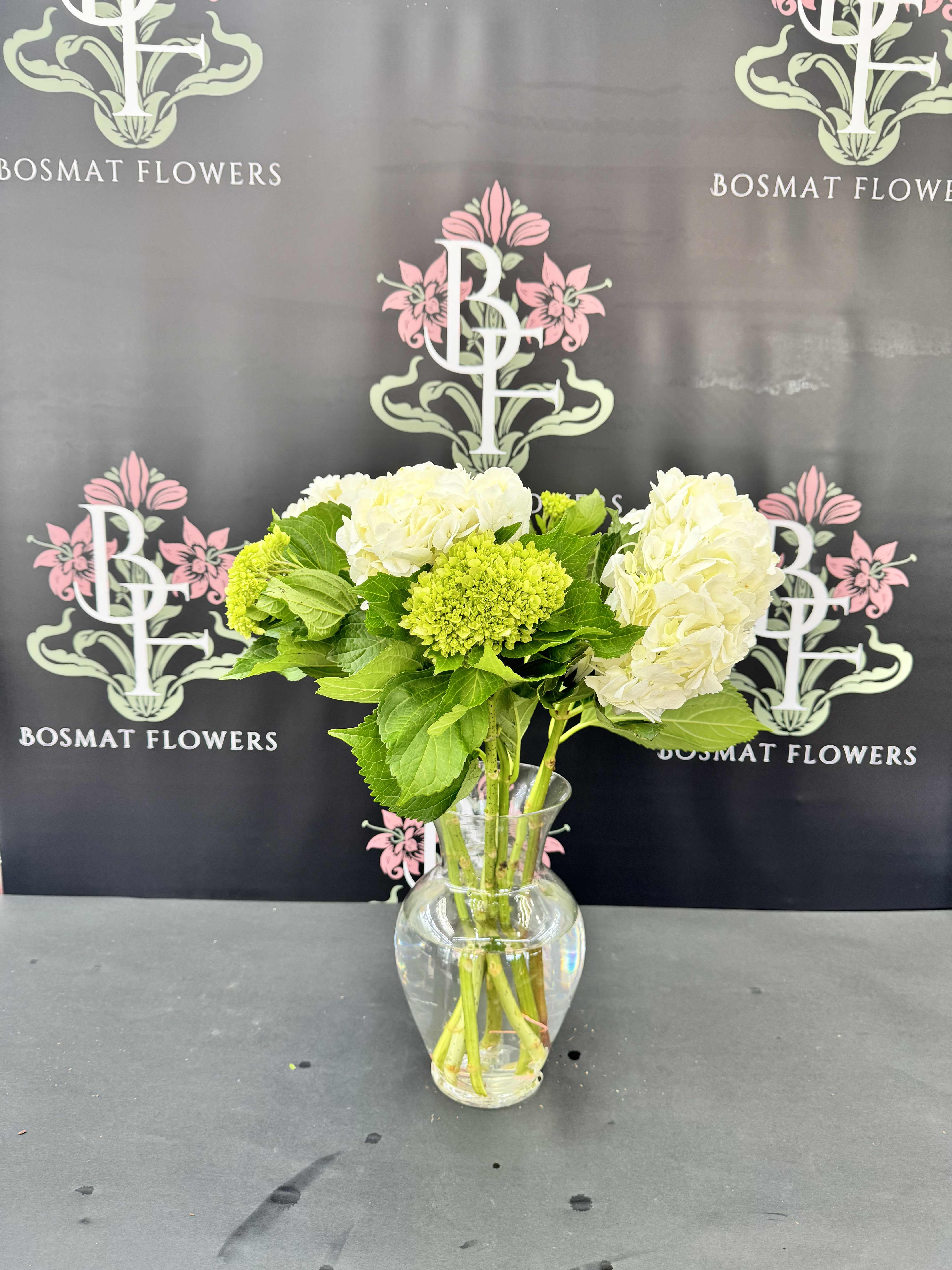White hydrangeas and green blooms in a clear glass vase