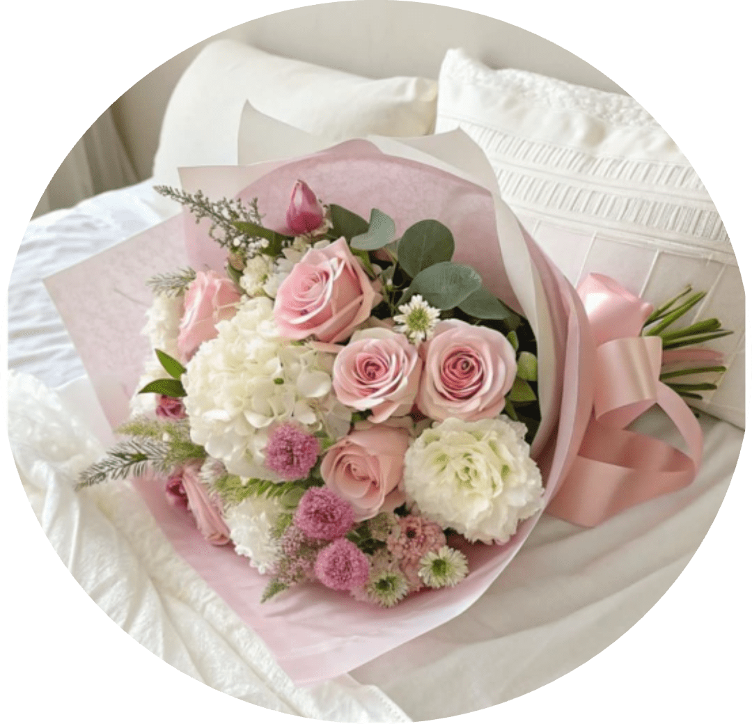 Playa Mansa - Blush pink roses nestled with creamy white hydrangeas create a soft, romantic birthday bouquet or anniversary gift that reads like a gentle embrace. This rounded hand-tied arrangement is ideal for weddings, Mother's Day, or any sentimental moment when the person you're thinking of should feel truly seen and cherished.  The bouquet pairs pale pink roses with clusters of white hydrangea-like blooms, delicate filler flowers, and eucalyptus-style greenery for muted contrast and texture. Wrapped in layered translucent pink and white decorative paper and finished with a wide satin ribbon, the presentation is polished and gift-ready. Choose this arrangement to send a feminine, airy message of love-available in a full, rounded size that arrives ready to display; trim stems and refresh water to keep blooms looking their best.