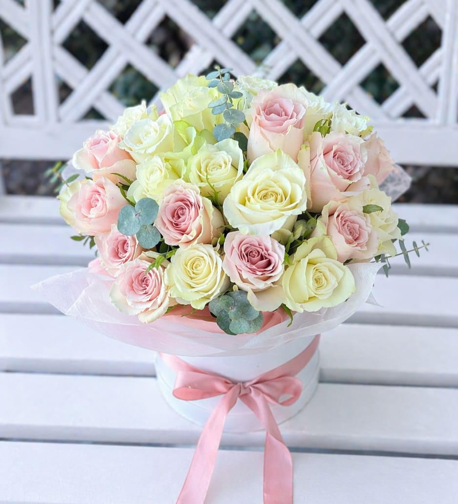 Bouquet of pale pink and cream roses in a white hatbox with a pink ribbon