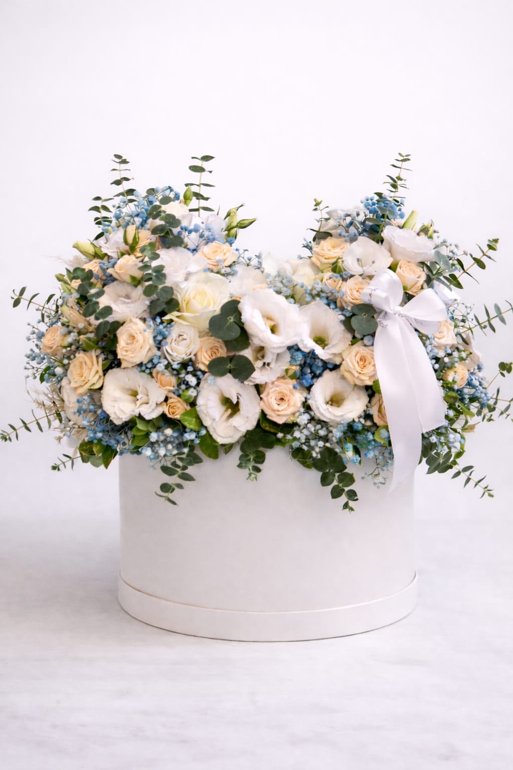 Low arrangement of white and peach flowers with blue accents in a round white hat box with ribbon