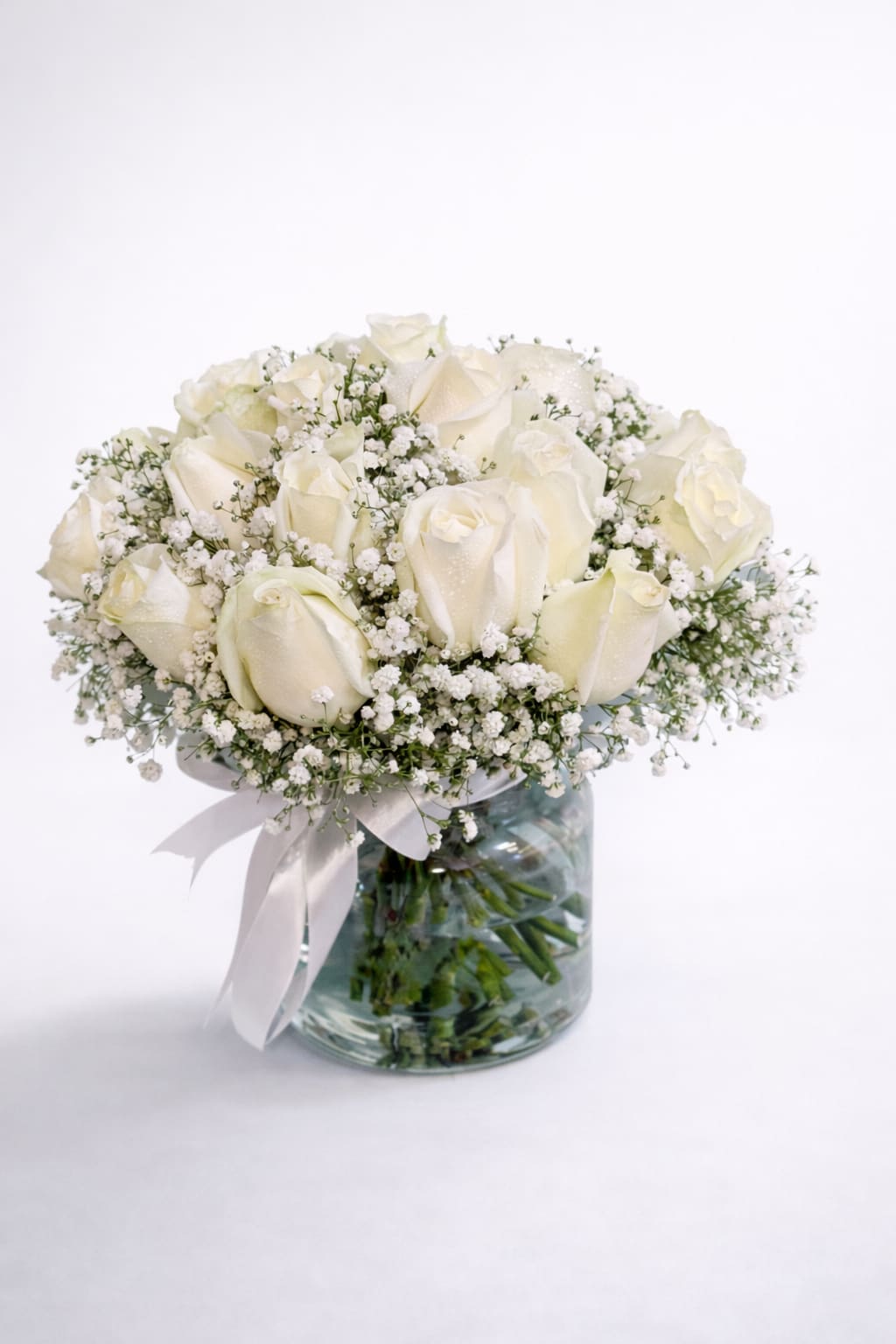 White rose bouquet in a glass vase with baby's breath and a ribbon