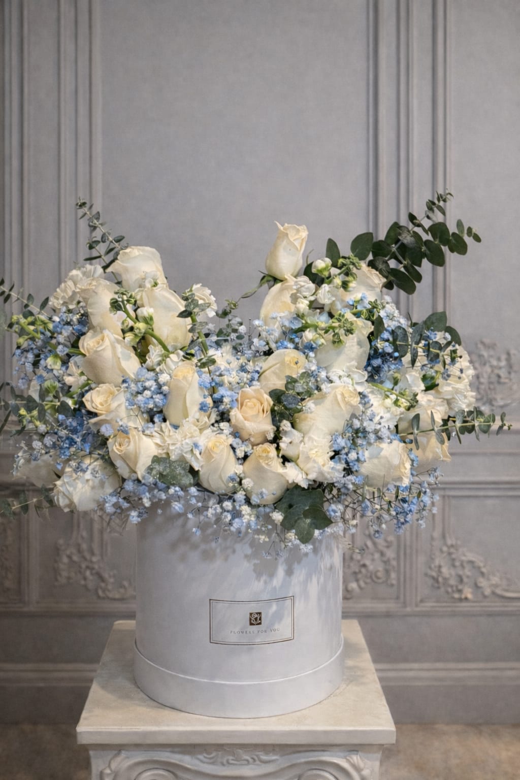 White roses and blue flowers arranged in a round hatbox