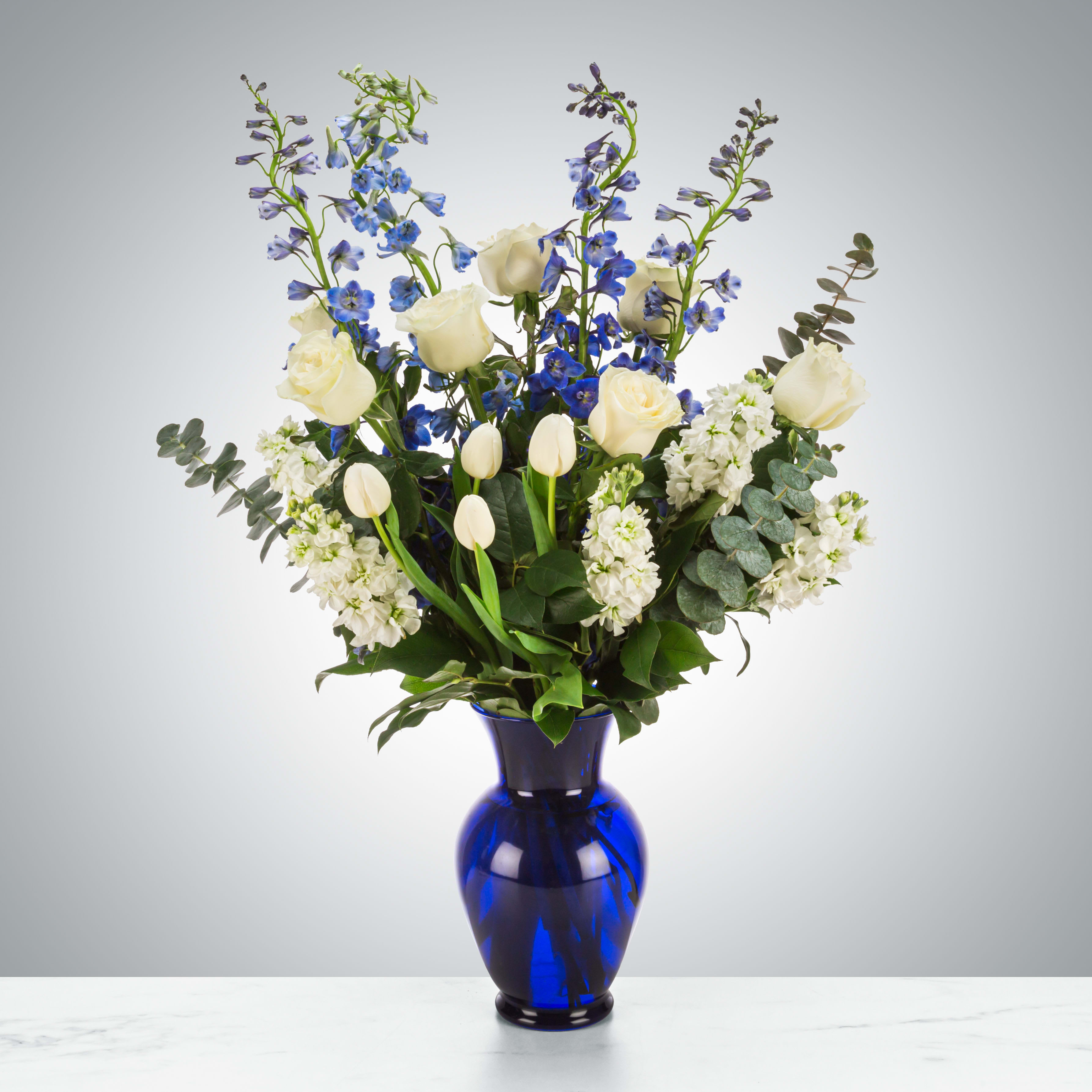 Orion's Belt by BloomNation™ - A blue and white arrangement featuring roses, tulips, and delphinium. Send this arrangement to anybody who likes stargazing or the night sky. A perfect gift to send for Hanukkah or the winter season.  Approximate Dimensions: 16"D x 28"H
