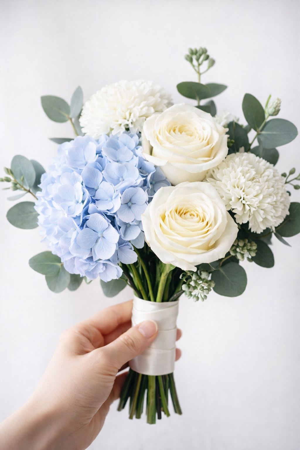Handheld bouquet of white roses, blue hydrangea, and white mums