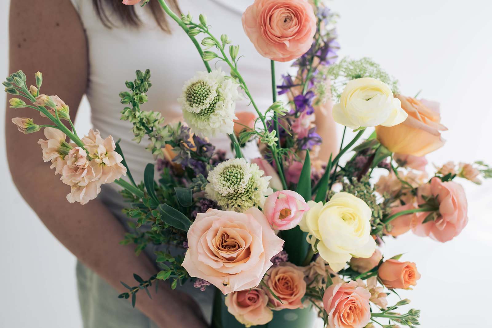 Handheld bouquet of peach, cream, and purple flowers