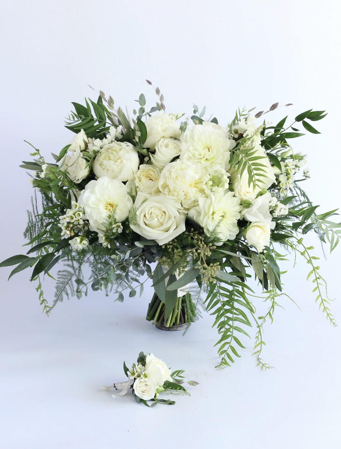 Large white rose and peony bouquet with trailing greenery and a matching white boutonniere.