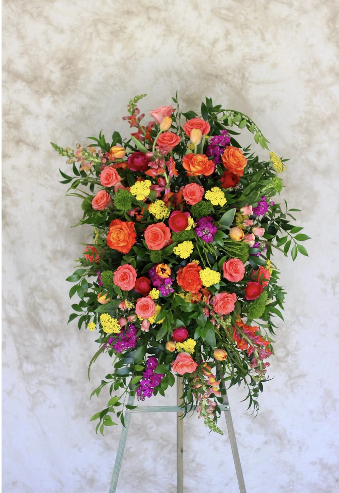 Bright standing spray of orange roses, yellow blooms, and pink and purple flowers on an easel