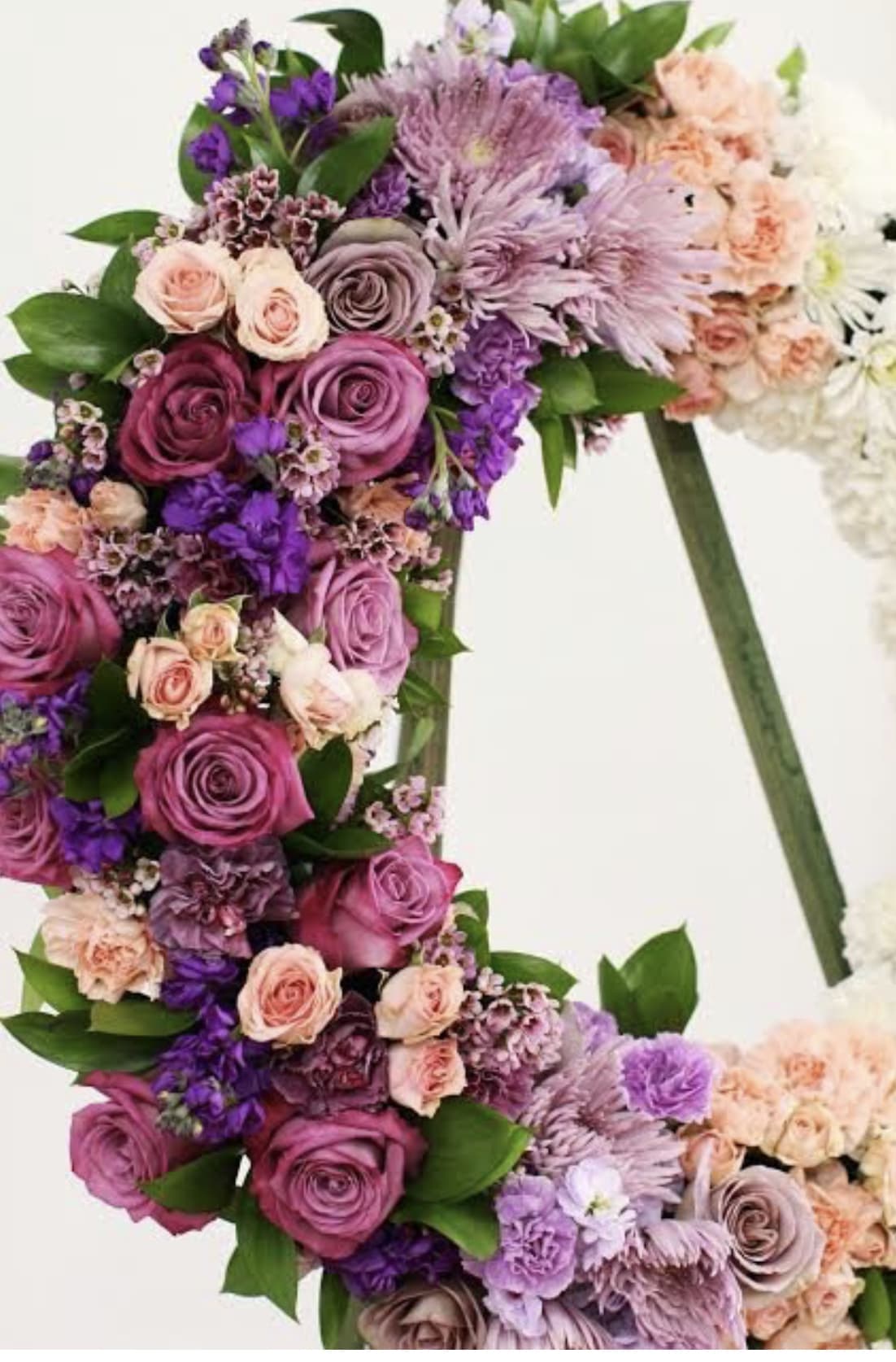 Standing wreath of pink and purple roses, carnations, and mums on an easel.