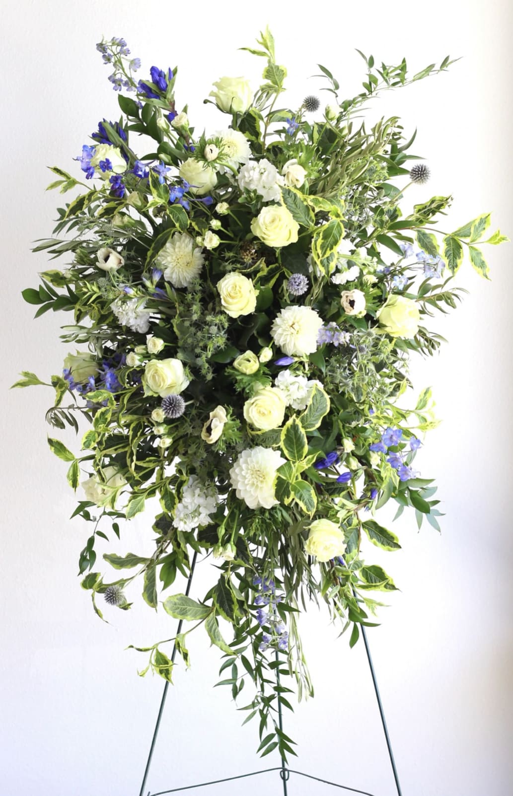 Tall standing spray of white and cream flowers with blue accents arranged on a metal easel