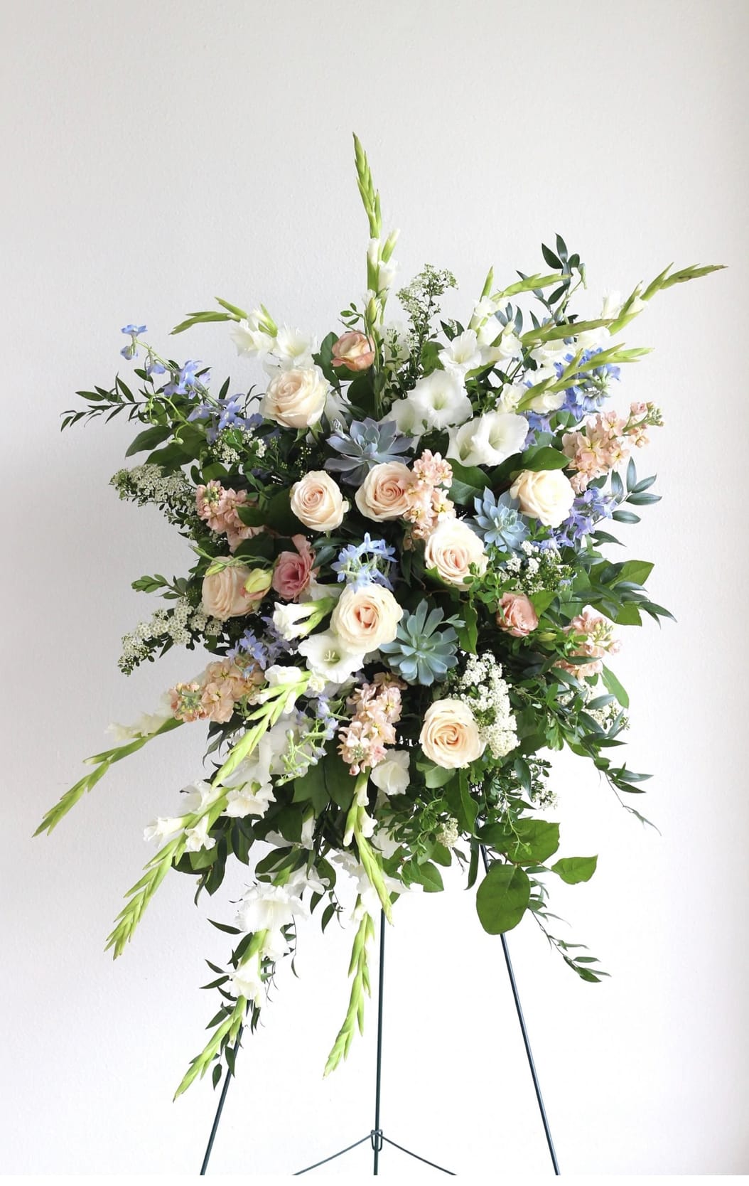 Tall standing spray of white, peach, and blue flowers arranged on a metal easel.
