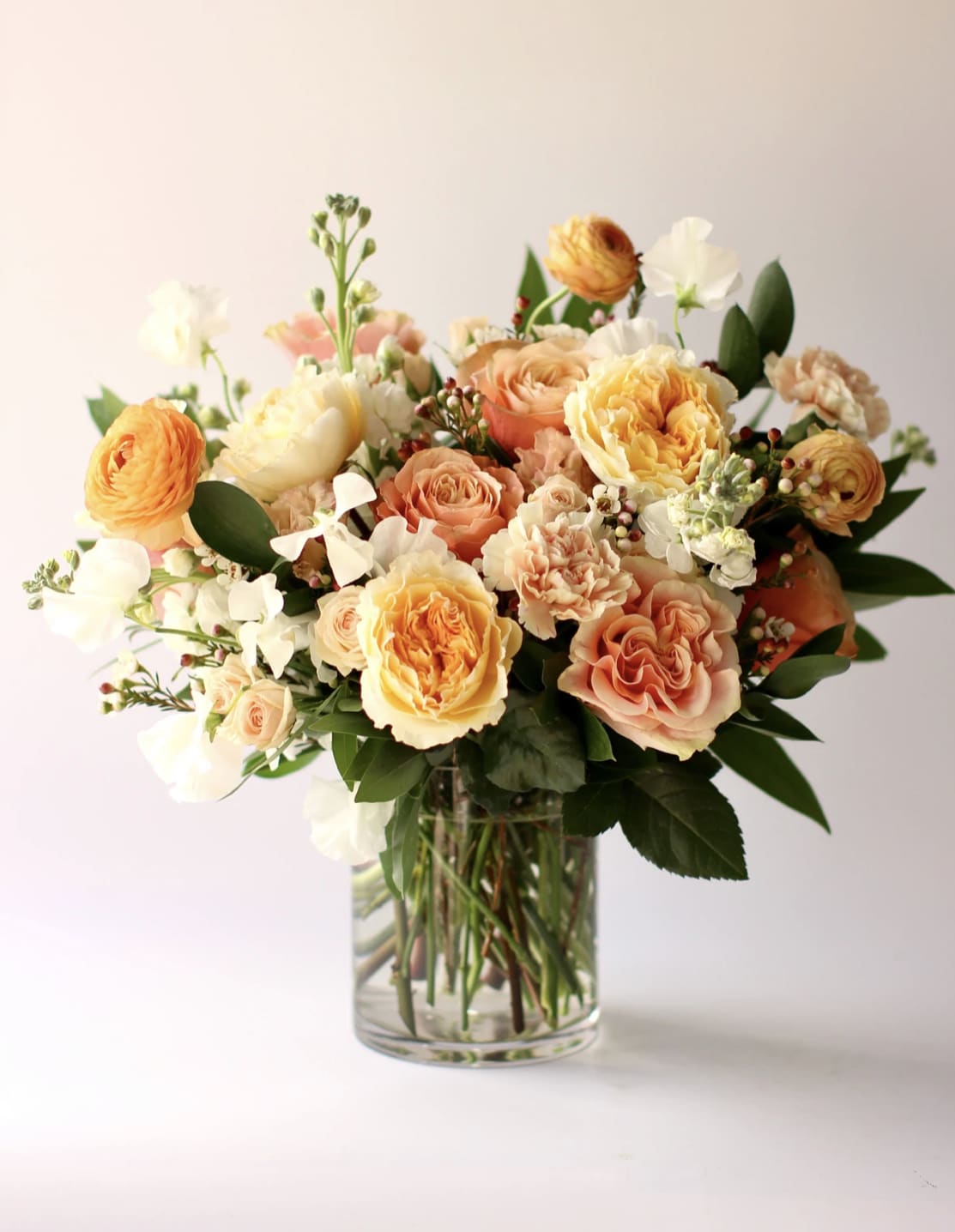 Peach and yellow rose arrangement with white accents in a clear glass vase.