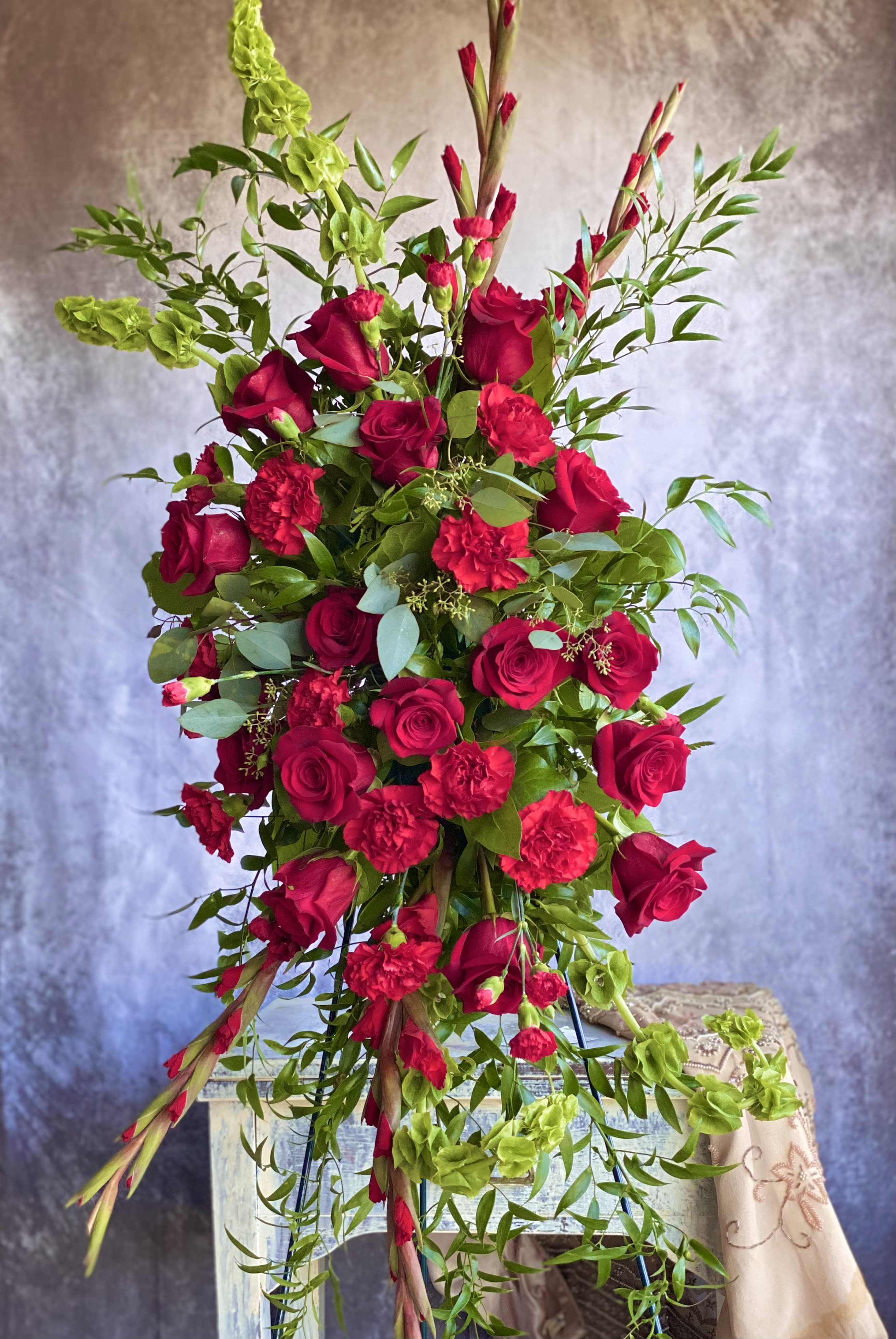 Tall cascading arrangement of red roses and carnations with green bells of Ireland.