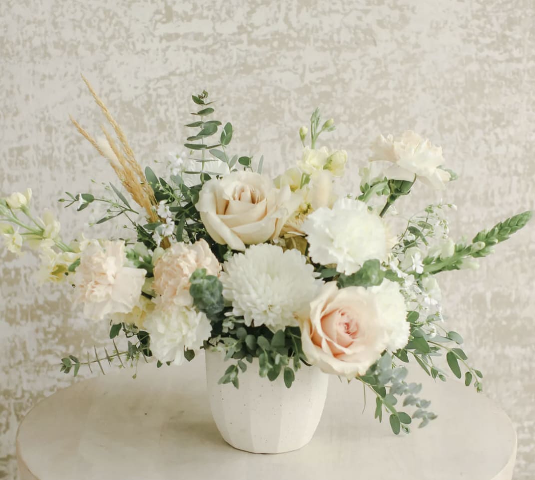 Low arrangement of cream roses, white mums, and peach carnations in a white pot