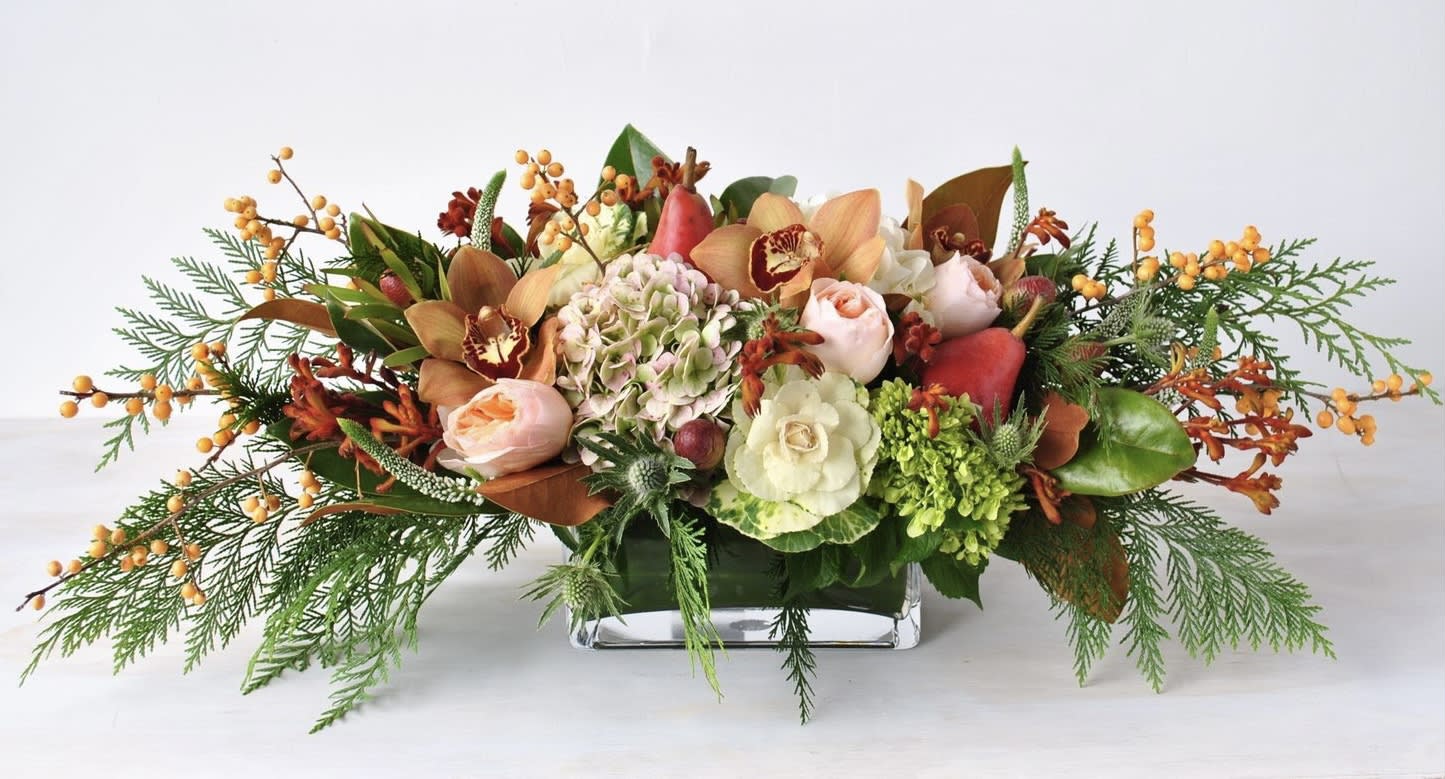 Low rectangular centerpiece with peach roses, orchids, hydrangea, berries, and evergreen accents in a glass vase