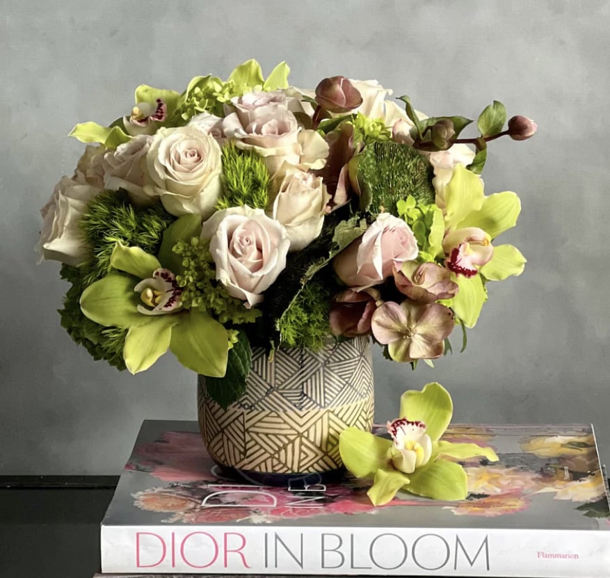 Compact arrangement of blush roses and green orchids in a patterned vase on books