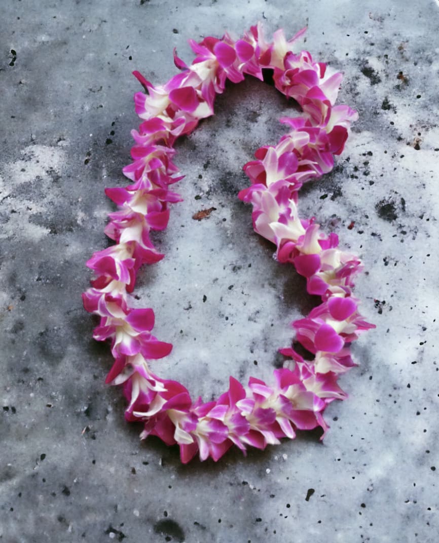 Purple and white orchid flower lei arranged in an oval on a gray stone surface