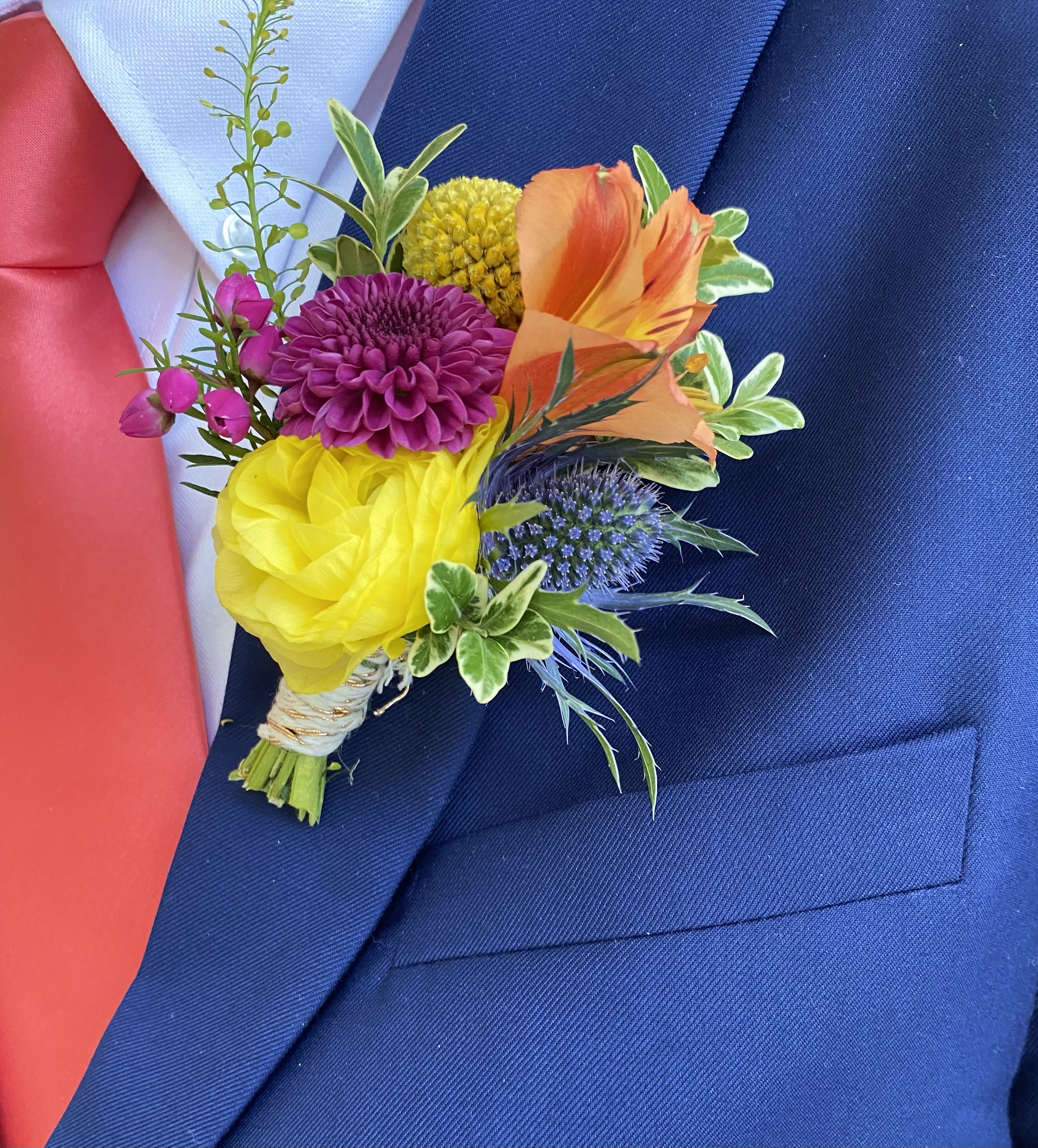 Colorful boutonniere with yellow, orange, purple and blue blooms on a navy suit jacket.