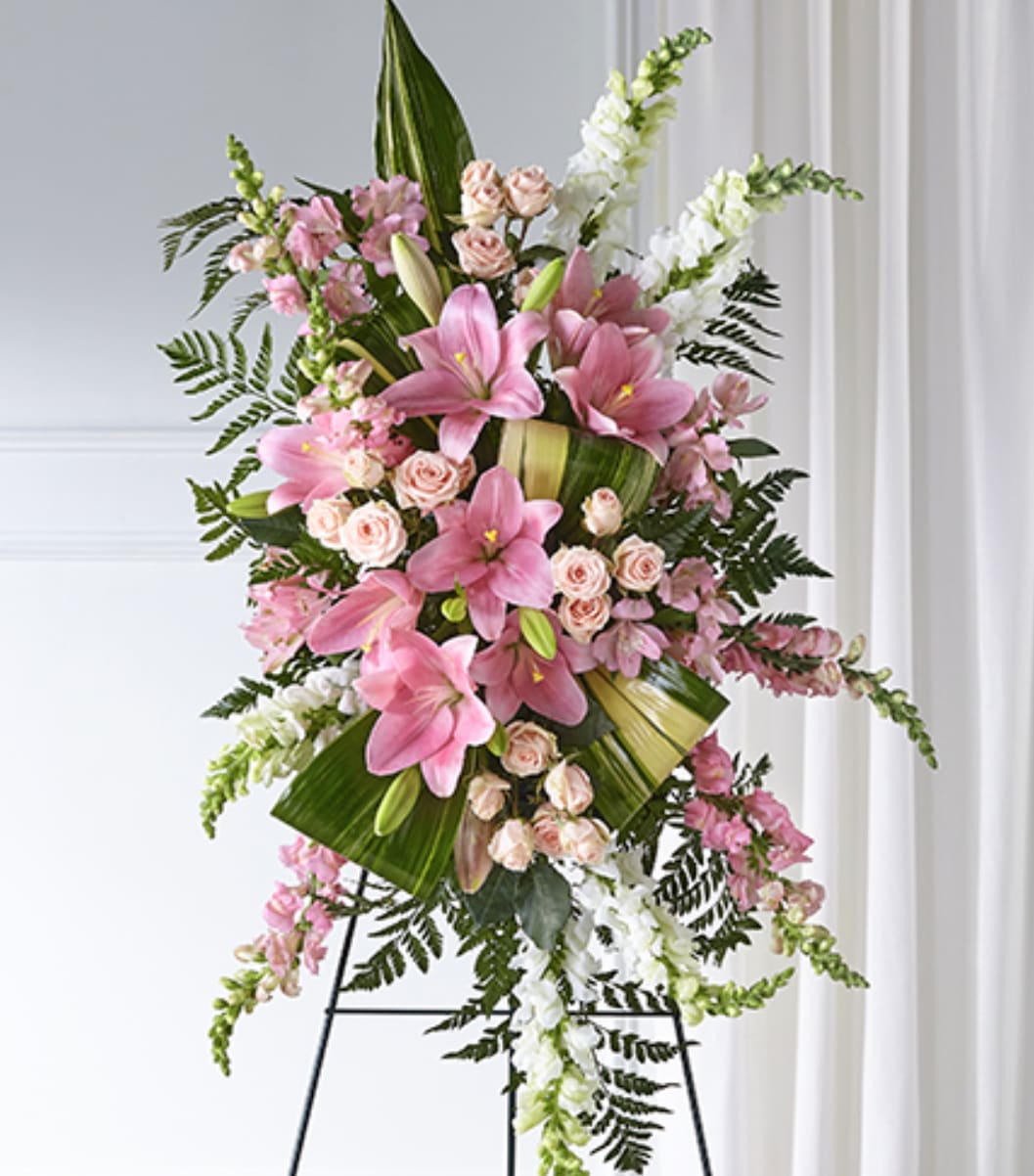 Tall standing spray with pink lilies, pale spray roses, and white snapdragons on a metal easel