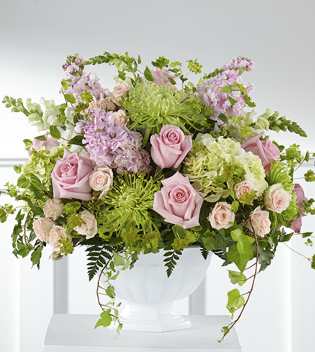 Large pastel arrangement with pink roses, green mums, and hydrangeas in a white pedestal bowl