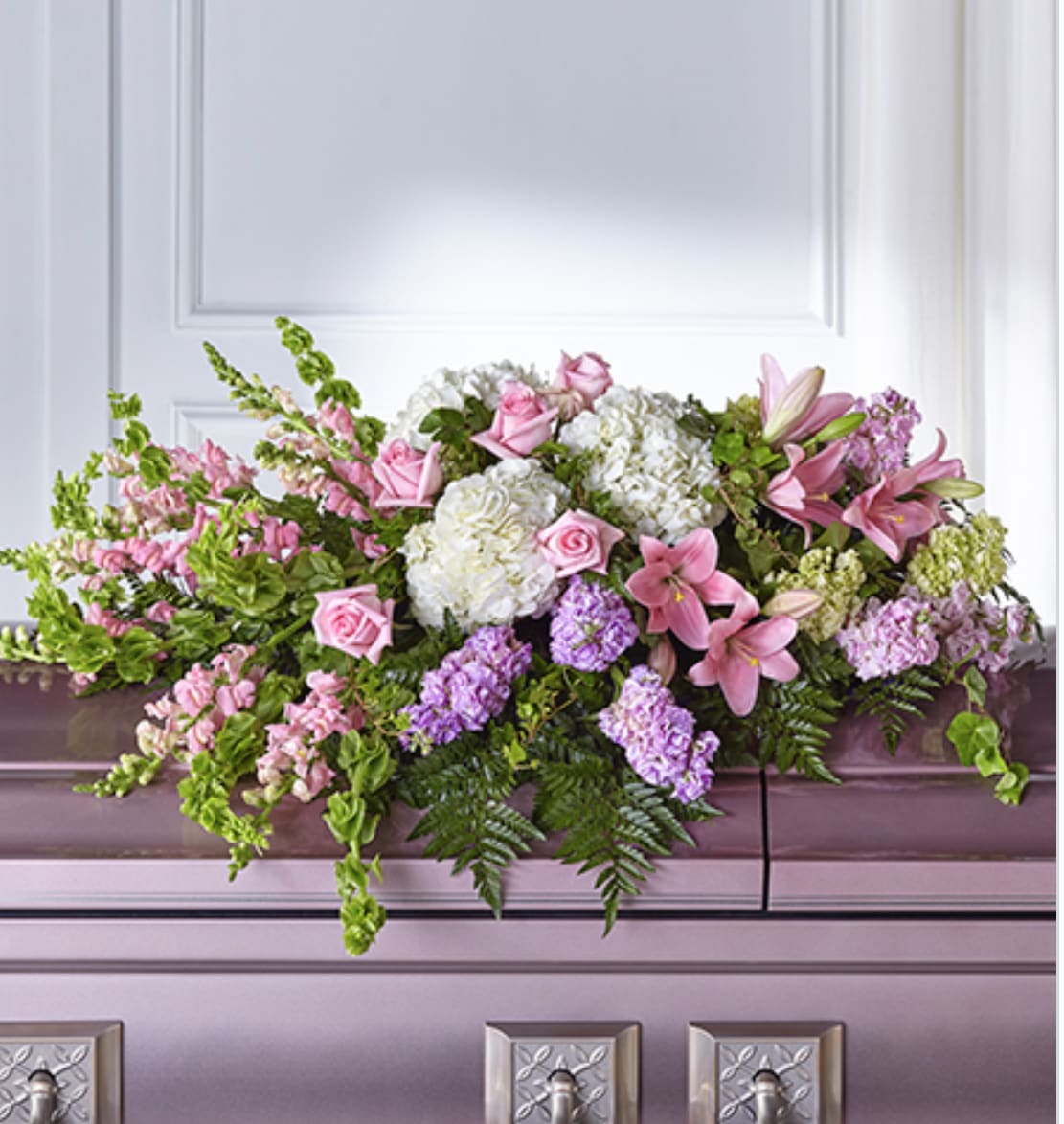 Pastel pink and white casket spray with roses, lilies, and hydrangeas on a lavender casket.