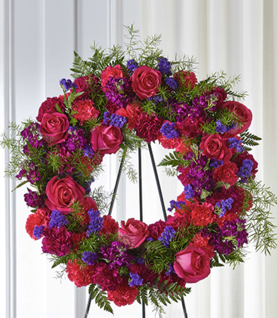Bright pink and purple standing wreath of roses and carnations on a black metal easel