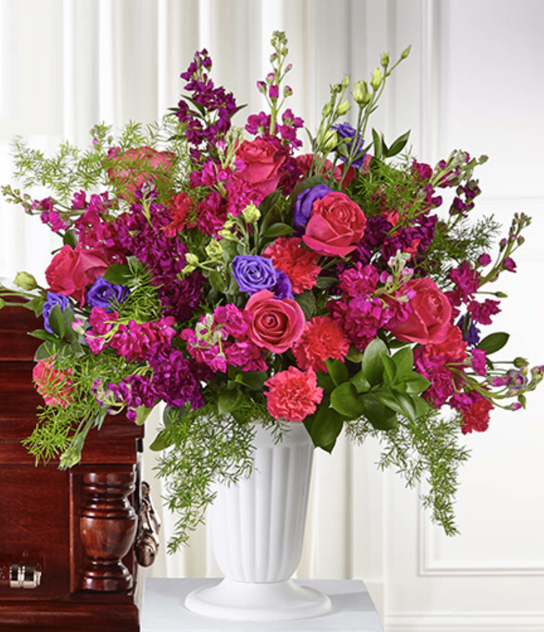 Tall pink and purple rose and carnation arrangement with trailing greenery in a white urn