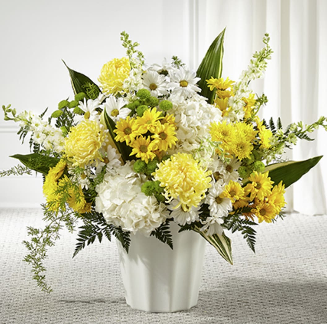 Yellow and white chrysanthemums, daisies, and hydrangeas arranged in a white vase.