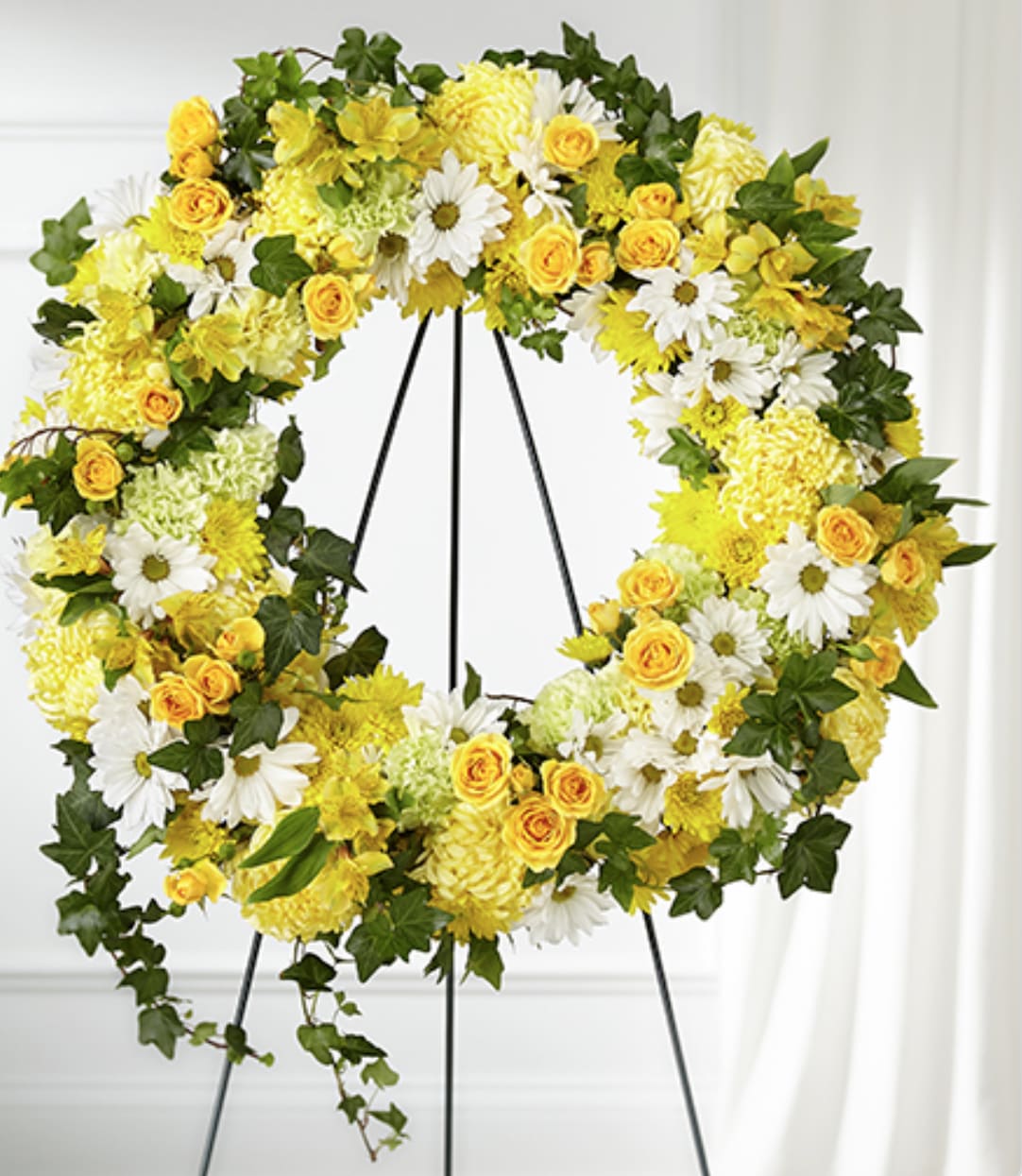 Large yellow and white floral wreath with ivy displayed on a metal easel stand