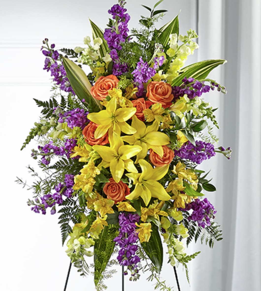 Tall standing spray of yellow lilies, orange roses, and purple flowers on a metal easel