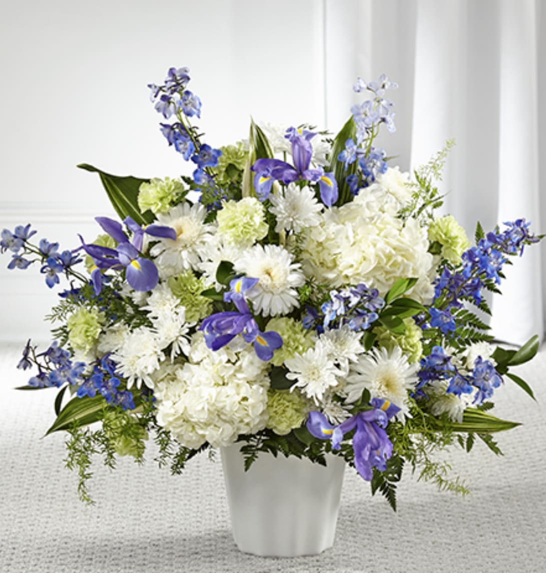 Tall arrangement of white hydrangeas, mums, green carnations and blue irises in a white vase
