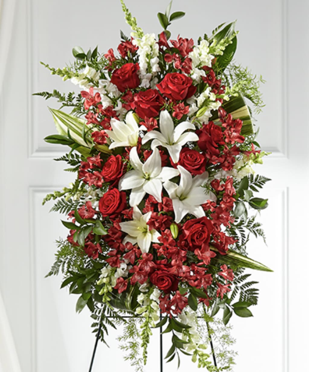 Standing spray of red roses, white lilies, and mixed red and white flowers on an easel.