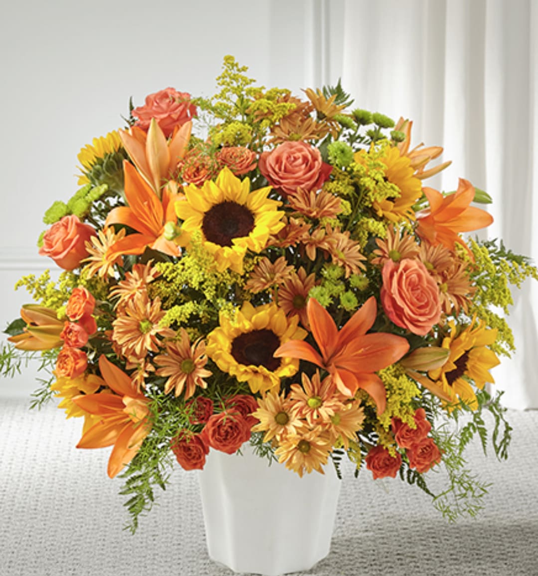 Large orange and yellow arrangement with sunflowers, lilies, roses, and mums in a white vase