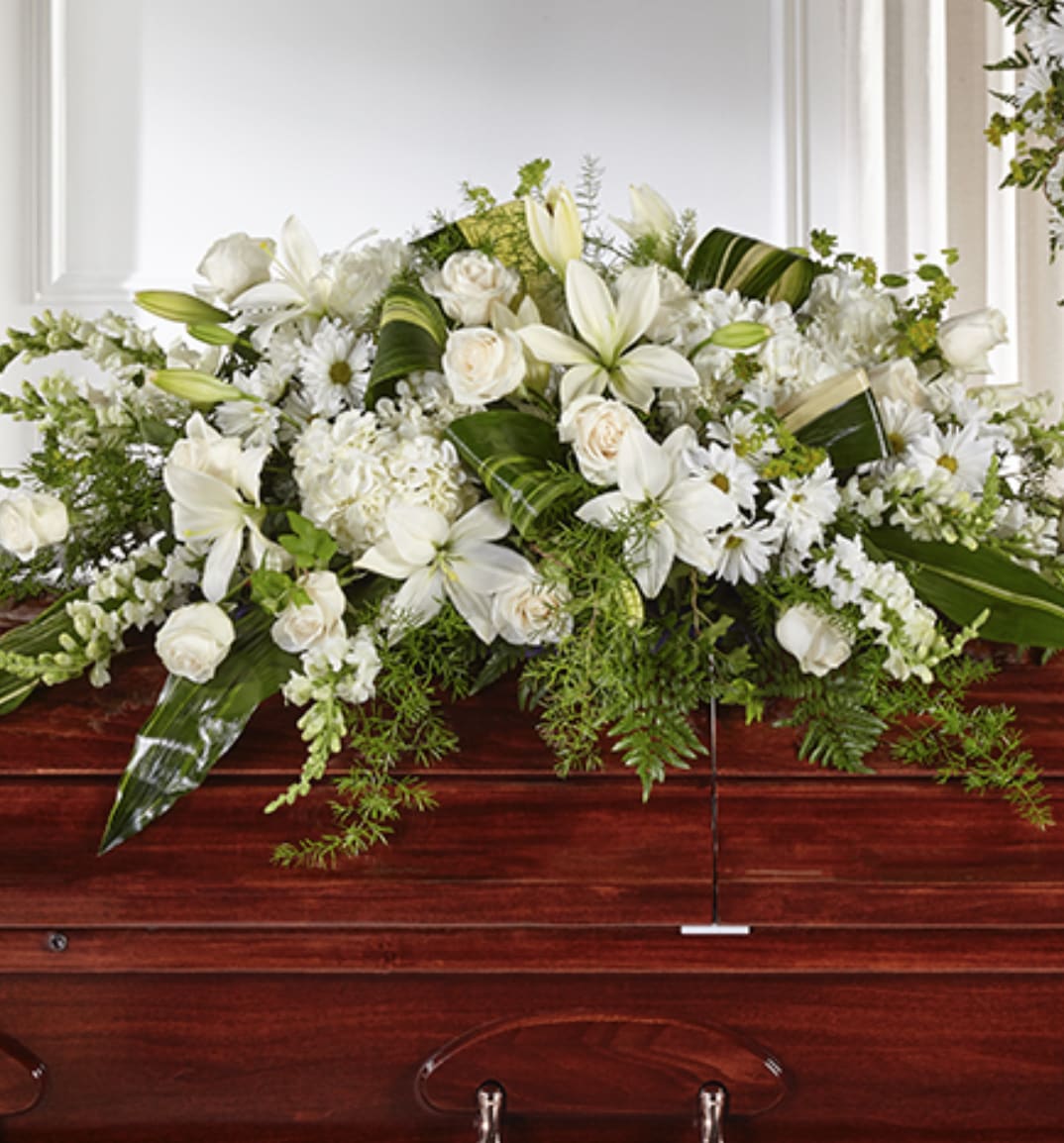 White lily and rose casket spray with mixed white flowers on a dark wood casket