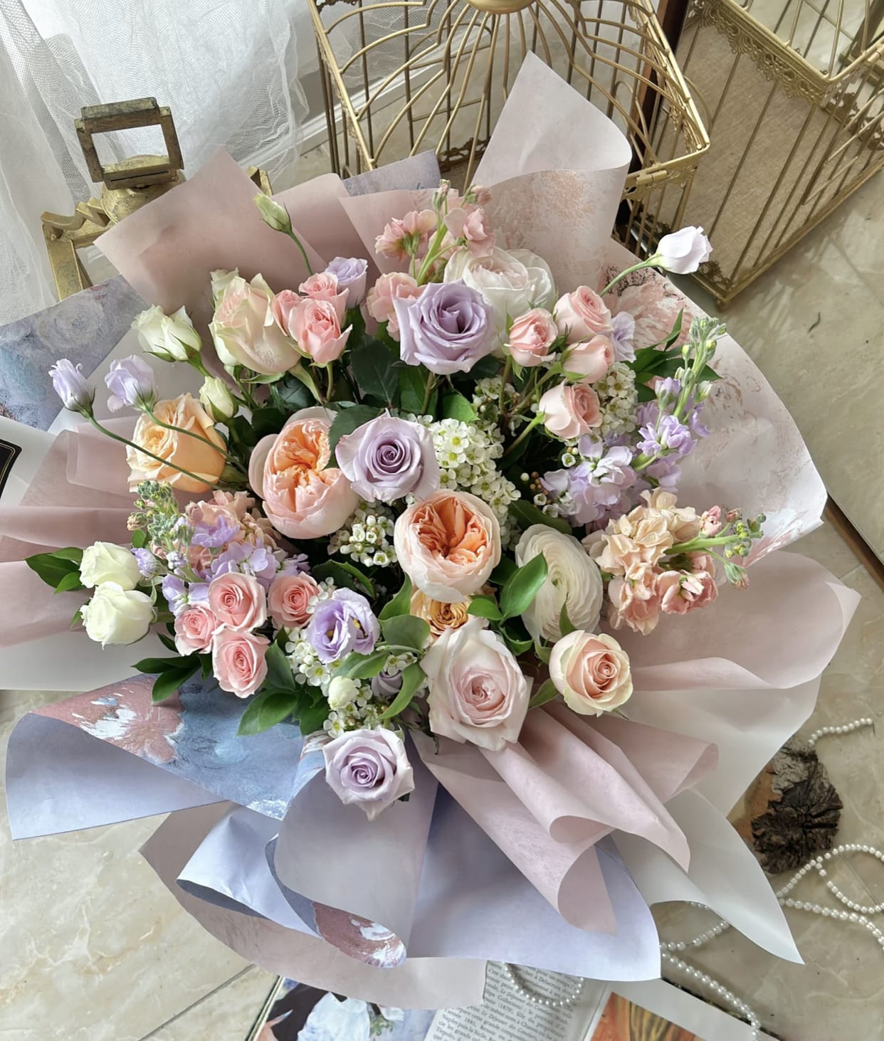 Pastel bouquet of pink, peach, and lavender roses with white accents wrapped in soft mauve paper