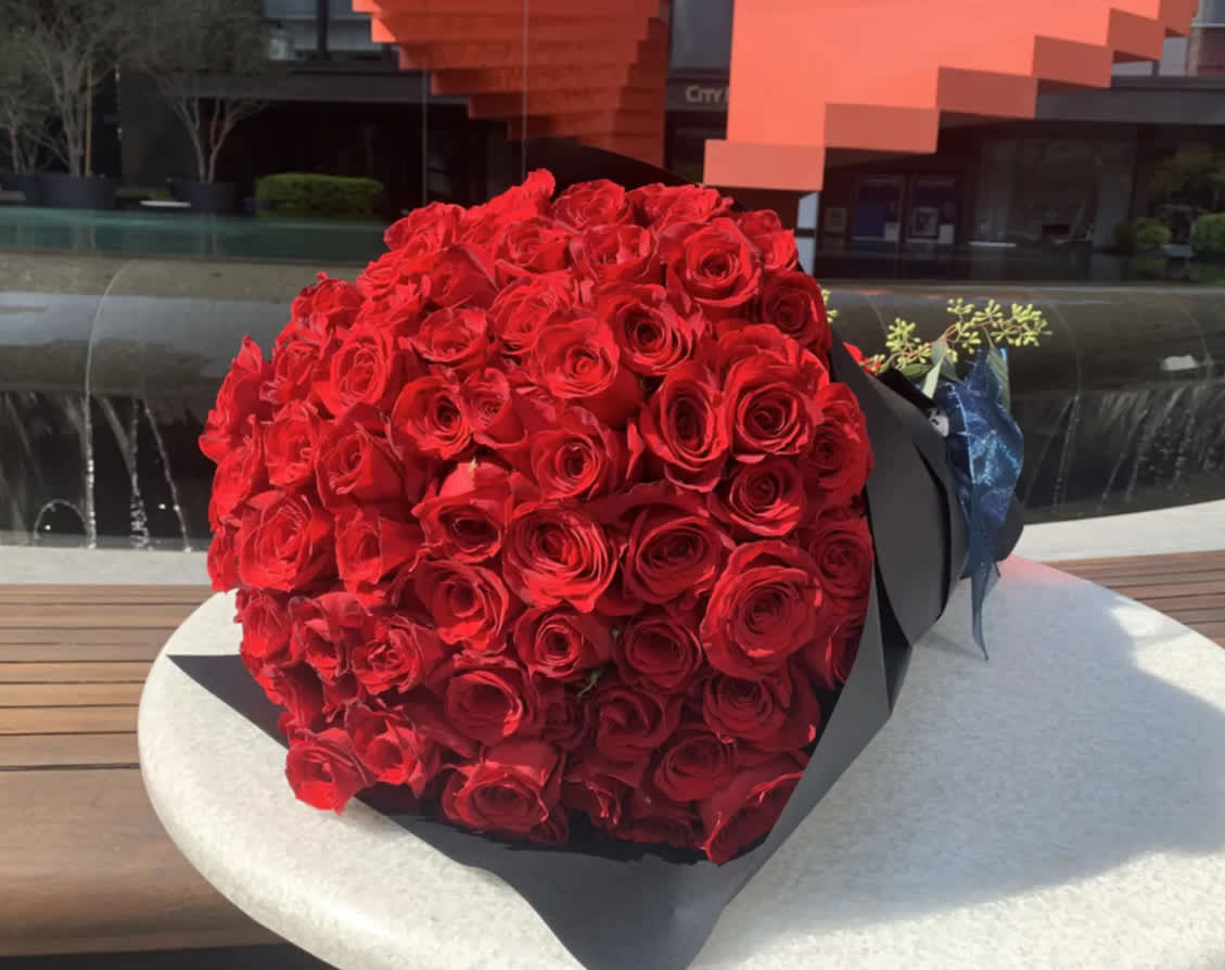 Large bouquet of tightly packed red roses wrapped in black paper with a blue ribbon