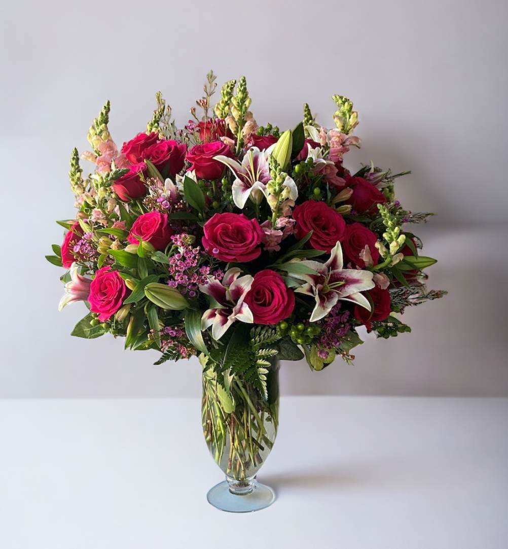 Tall arrangement of hot pink roses and white lilies in a clear glass vase