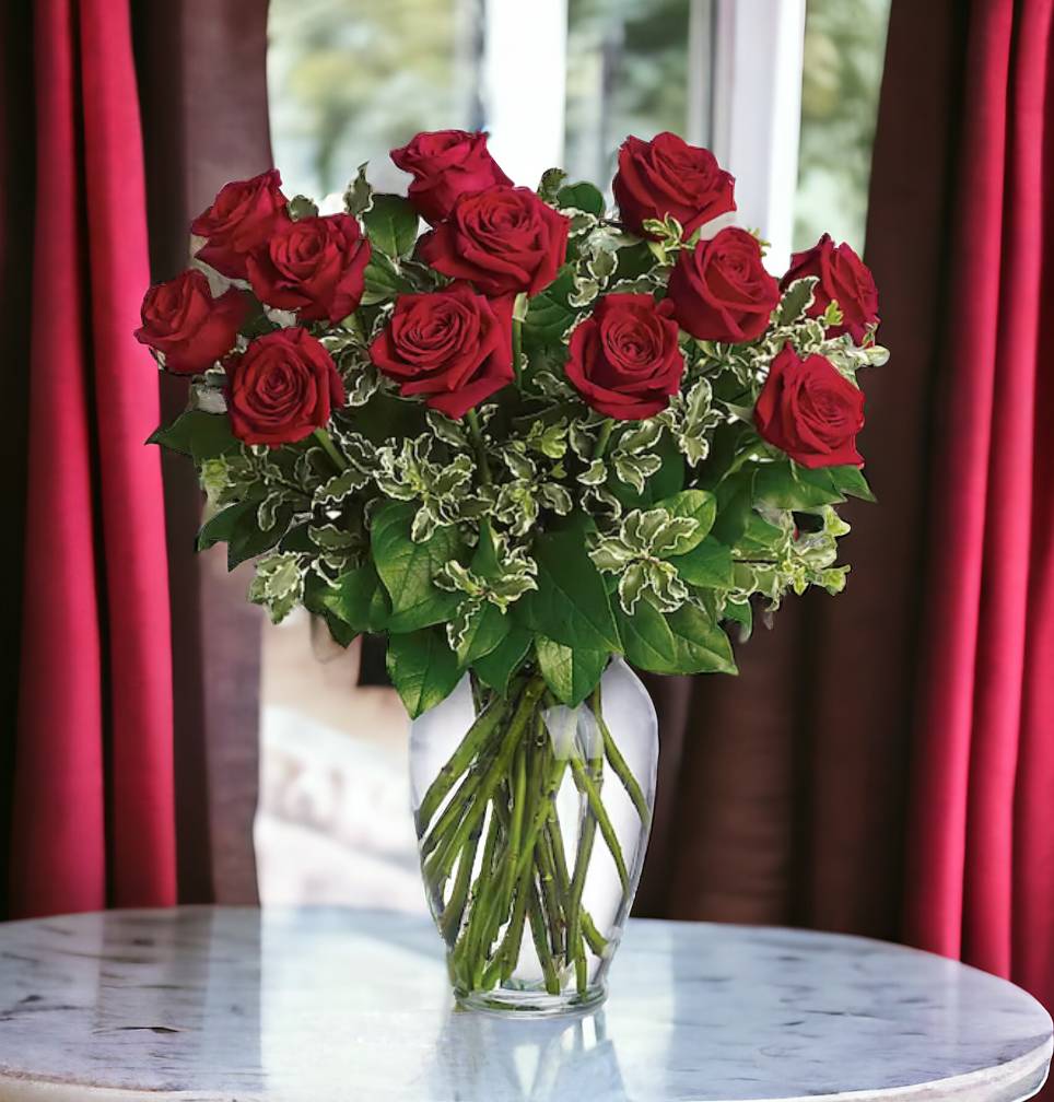 Tall arrangement of red roses in a clear glass vase on a round marble table.