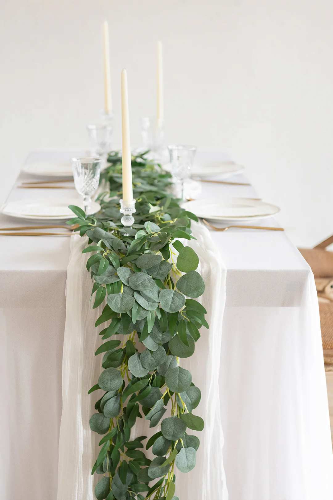White table with a long eucalyptus greenery garland and tall ivory taper candles.