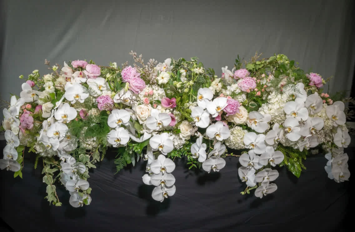 Long cascading arrangement of white orchids with pink and ivory blooms on a dark surface