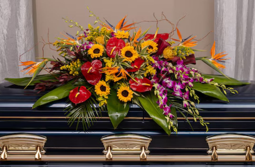 Tropical casket spray with yellow sunflowers, red blooms, purple orchids, and orange birds of paradise.