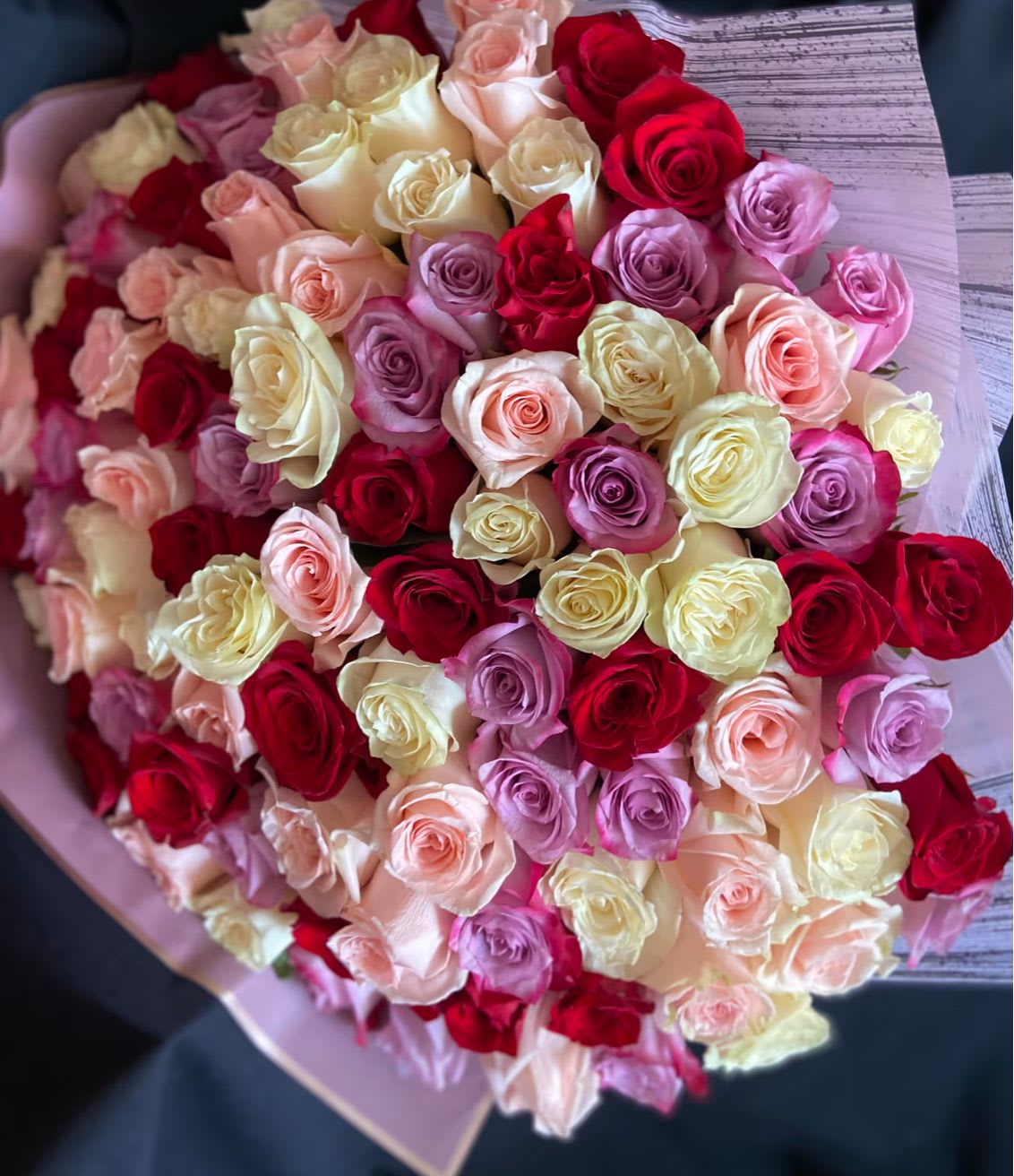 Large bouquet of red, cream, peach, and lavender roses wrapped in pastel paper