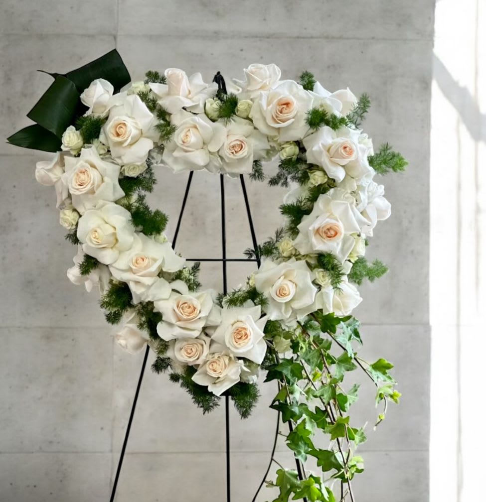 Heart-shaped wreath of white roses with trailing ivy on a black easel stand